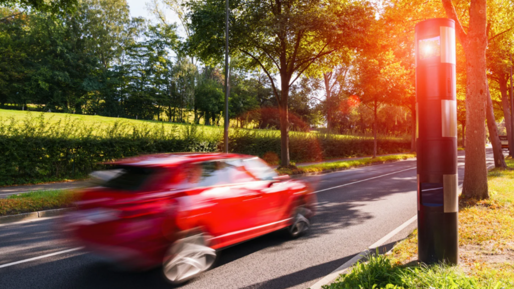 Rotes Auto wird von einem Blitzer erfasst – Symbolbild für Punkte in Flensburg wegen Geschwindigkeitsüberschreitung -ein punkt in flensburg