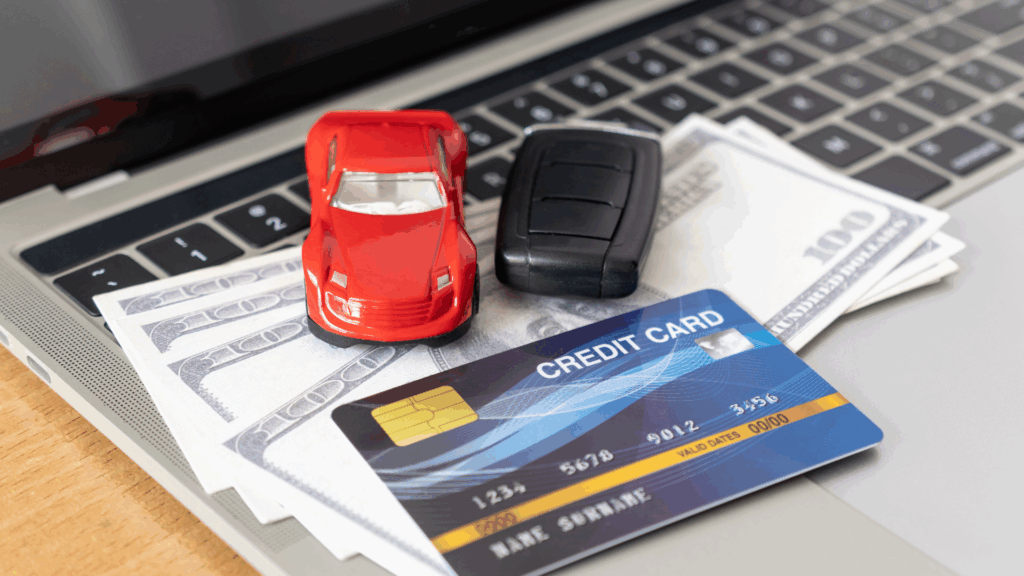 Symbolbild zur Punkteauskunft in Flensburg: Spielzeugauto, Kreditkarte und Geld auf Laptop