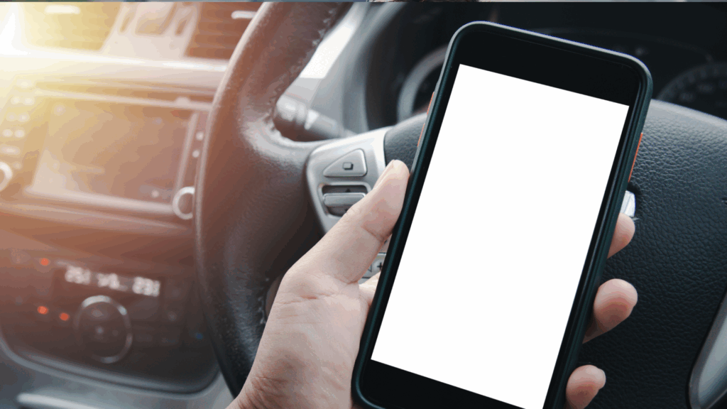 Eine Hand hält ein Smartphone vor dem Lenkrad während der Fahrt Symbolbild für Ablenkung im Straßenverkehr und Punkte im Verkehrsregister